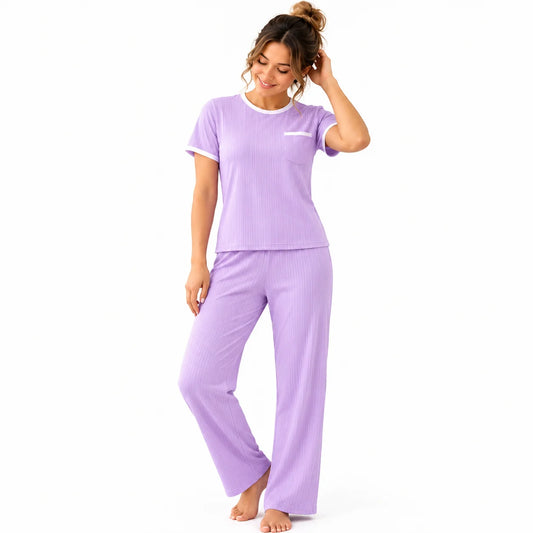Mujer luciendo pijama lila de tela rib acanalada, con blusa de manga corta, bolsillo frontal con ribete blanco y pantalón largo, en una habitación de tonos claros.